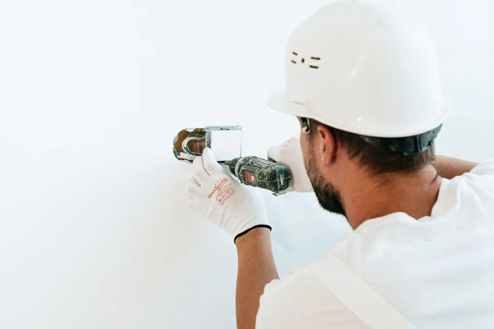 Técnico com capacete e luvas usando uma ferramenta elétrica em uma parede