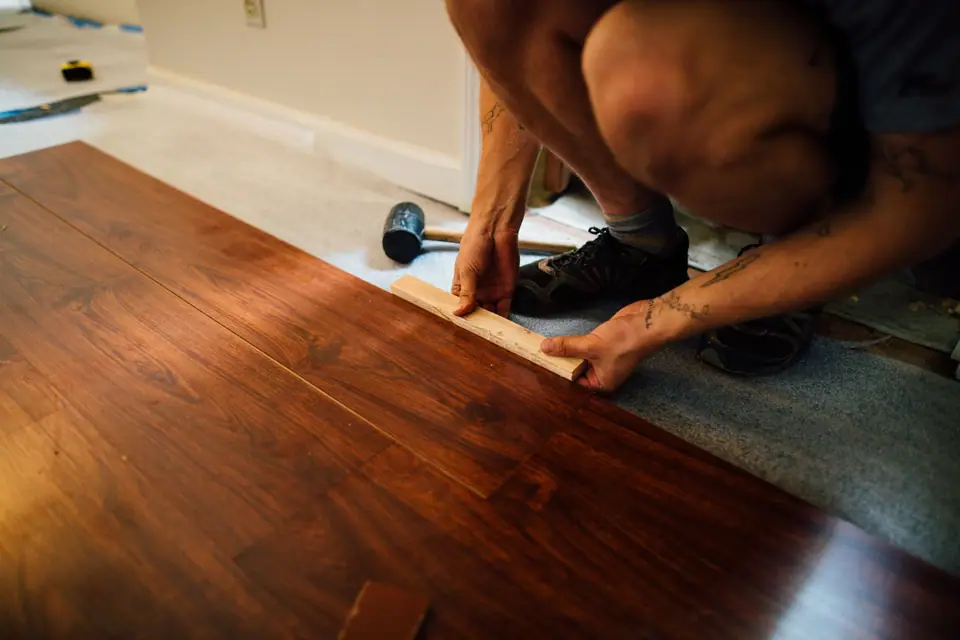 Profissional instalando piso laminado de madeira com martelo de borracha