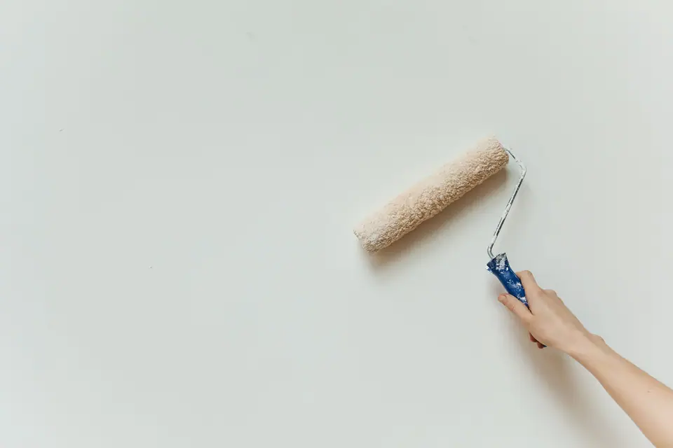 Detalhe de uma mão pintando uma parede branca com rolo
